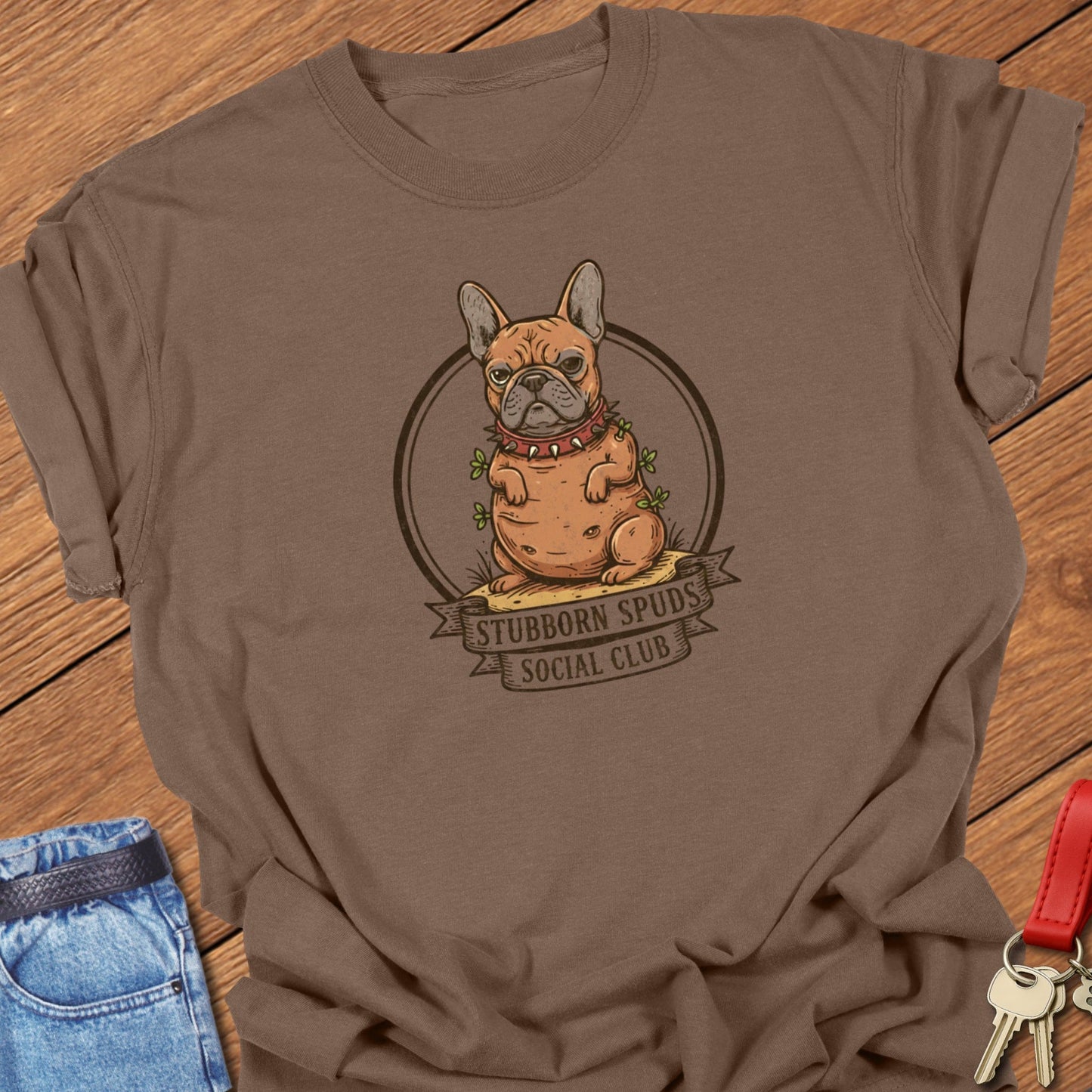 French bulldog illustrated as a potato mascot with “Stubborn Spuds Social Club” banner design printed on espresso Comfort Colors t shirt.