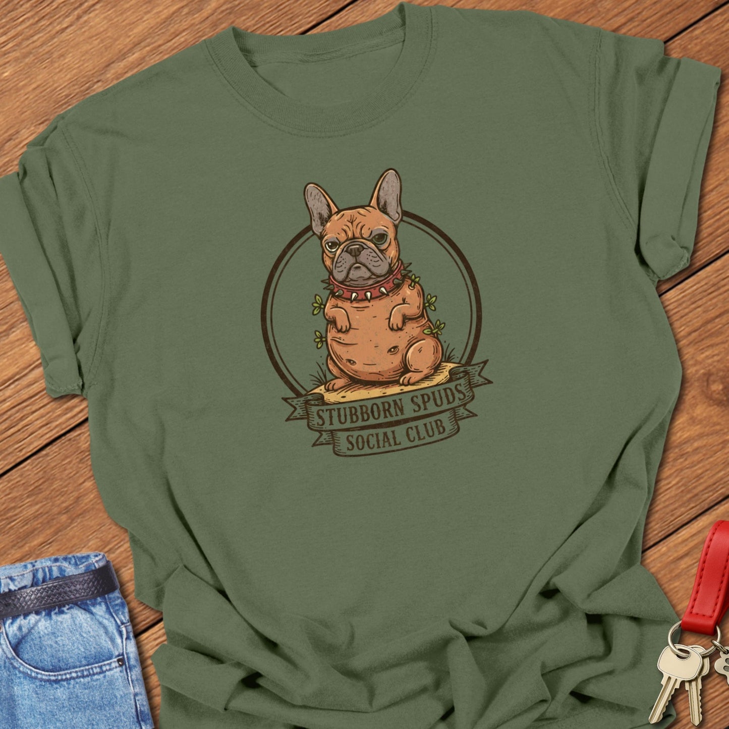 French bulldog illustrated as a potato mascot with “Stubborn Spuds Social Club” banner design printed on moss Comfort Colors t shirt.